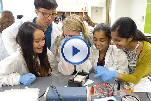 A group of students in lab coats looking at an electronic device.