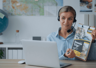 A woman wearing headphones holding a book and sitting at her desk.