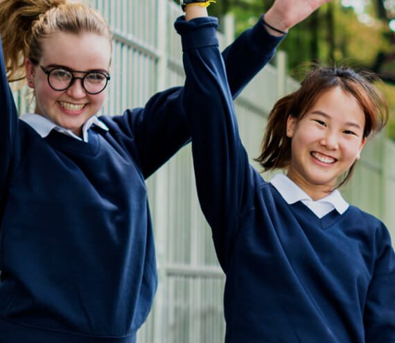Two girls in school uniforms holding hands and smiling.