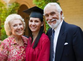 A woman in graduation gown with an older man and woman.